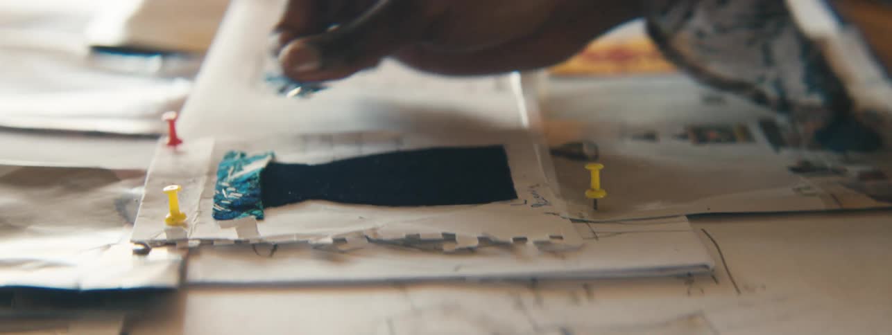 Female hand placing a piece of fabric on top of a fashion drawing