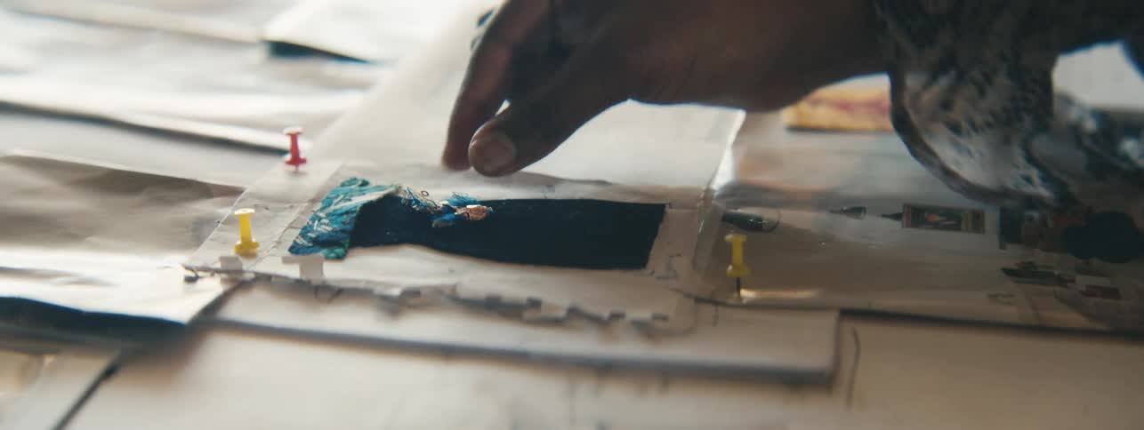 Closeup of a designers hand carefully placing jewelry on miniature dress sketches
