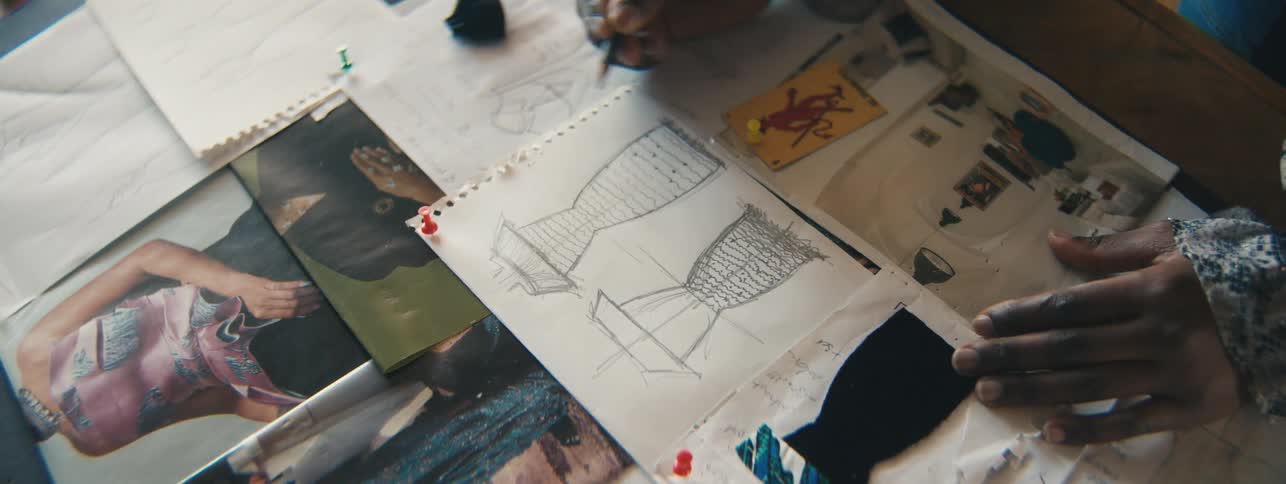 The hands of a person using a pencil to draw something on a white paper