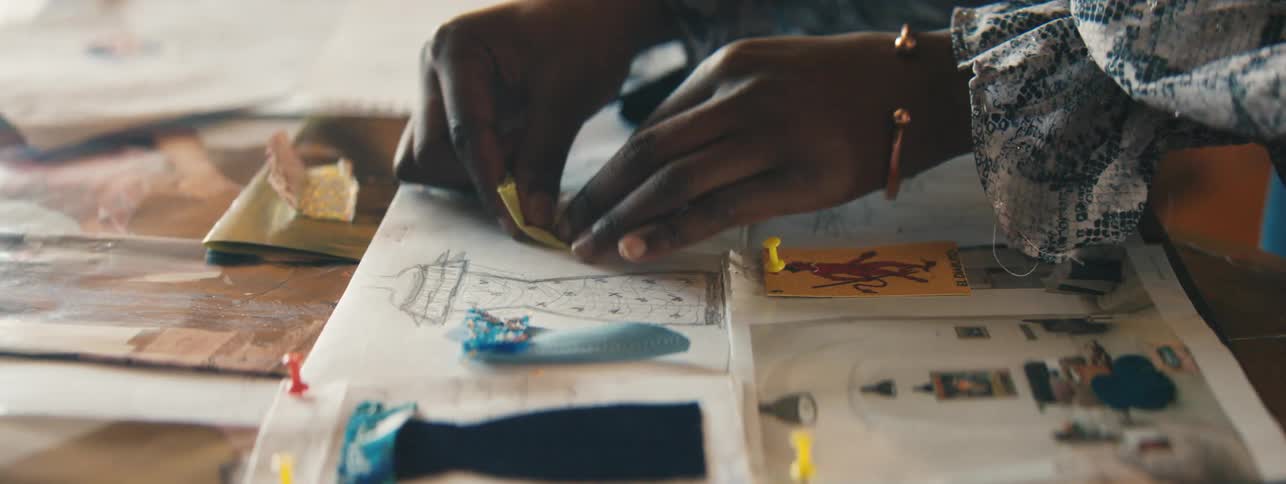 Closeup of a designers hand carefully placing jewelry and samples of clothes over miniature dress sketches