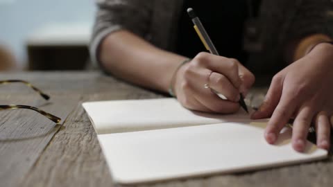 Caucasian person draws with a pen in a notebook