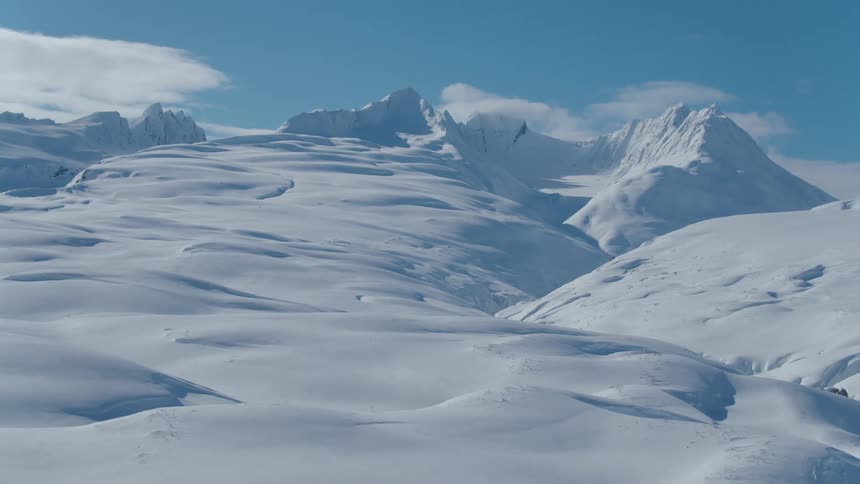 A vast snowy mountain landscape with snowcapped peaks rising against a clear blue sky