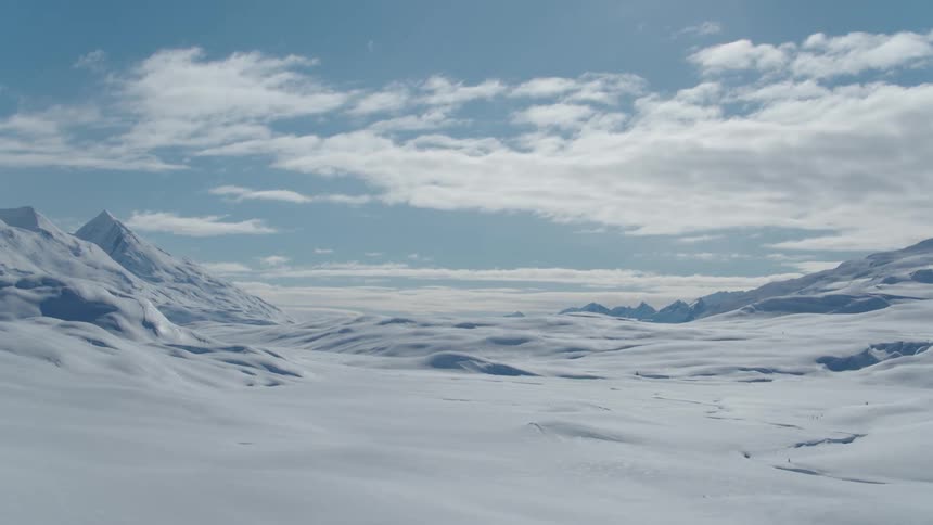 Snowy mountains tower over snow covered plains on a cloudy winter day