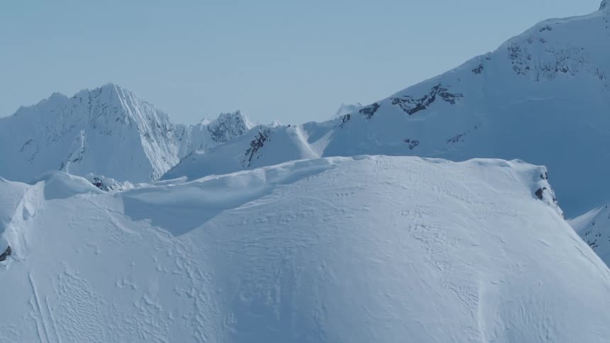 A peak of a large mountain covered in snow and behind it there are some even larger mountains
