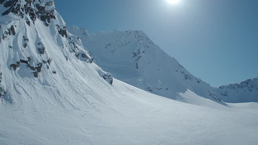 A mountain range with mountains and ground covered in snow and strong sunlight coming from the sky that is clear and blue