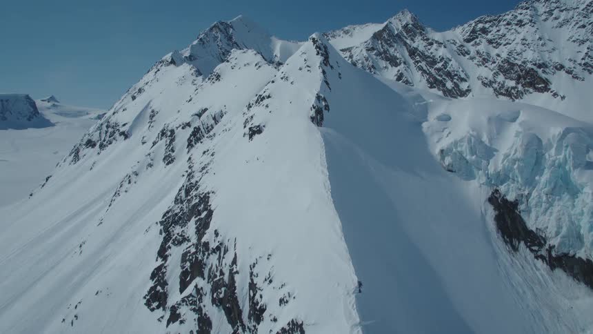 Aerial of snow capped mountain peaks under blue skies