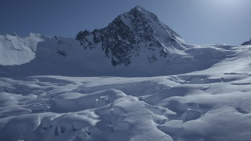 A completely white ground of thick snow with some holes and there is a mountain of rocks behind