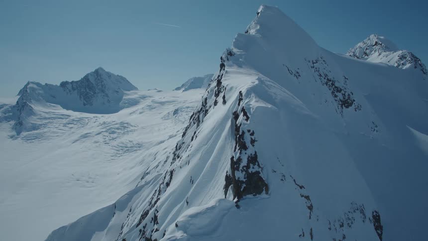 The peak of a large snowcapped mountain in a mountain range on a day with a blue sky