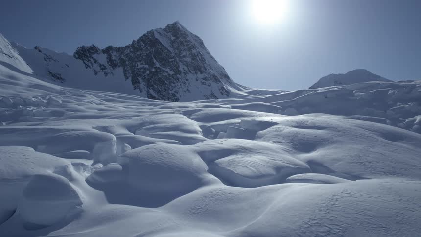 Layers of snow with mountains in the background and the strong sun