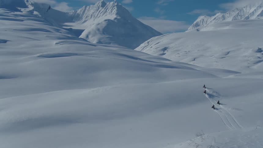 People ride snowmobiles up a snowy slope near the mountains