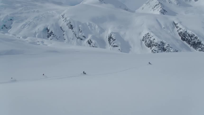 Aerial view of snowmobiles driving on a vast snowy landscape with mountains in the distance