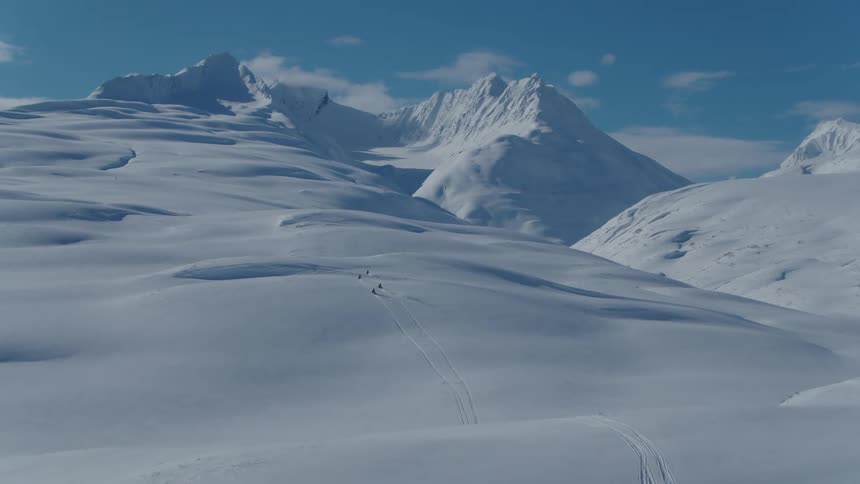 An aerial clip of an arctic mountain range with four ski riders
