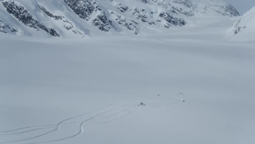 Small group of people riding snowmobiles in a snow covered field with mountains in the background