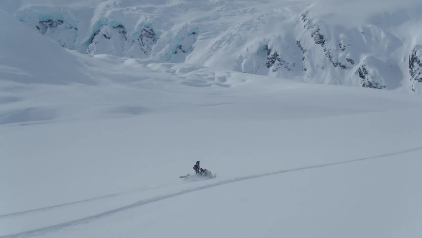 Two people on snowmobiles crossing a snow covered valley