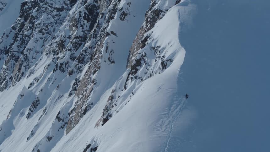 An aerial view of a person climbing a huge snow mountain and leaving a trail wherever he goes