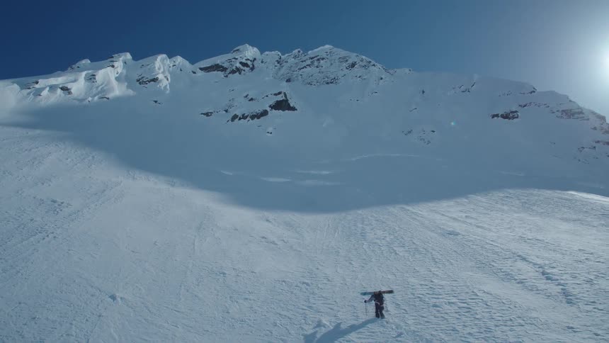 A lone snowboarder traverses a snow covered mountain slope