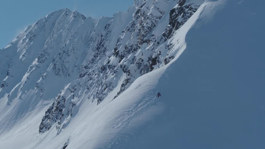 A person climbing a steep slope on a snow covered mountain under a blue sky