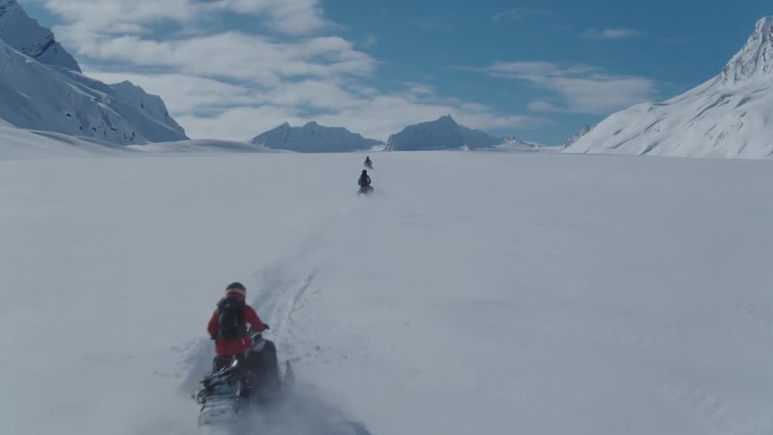 People ride snowmobiles across a snowy plain between mountains during winter