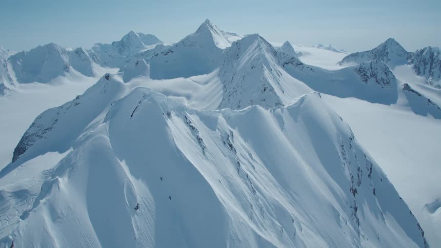 A large mountain range with mountains covered in white snow and contrasting with a clear blue sky