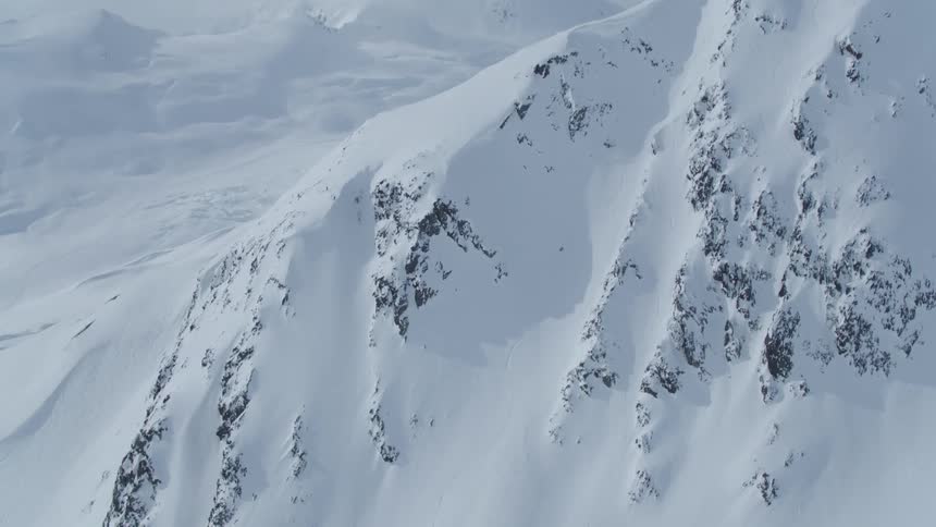 An aerial view of a large snowcovered mountain and a person skiing down it