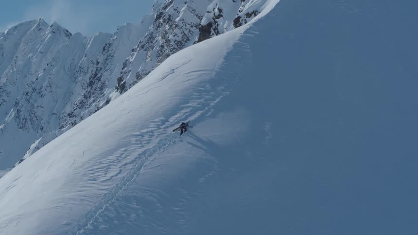 A skier traverses a steep snow covered slope in a mountainous region