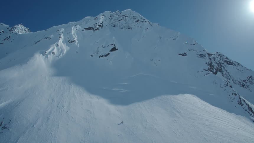 Aerial of a skier skiing down a mountain range in the back country on a blue bird day