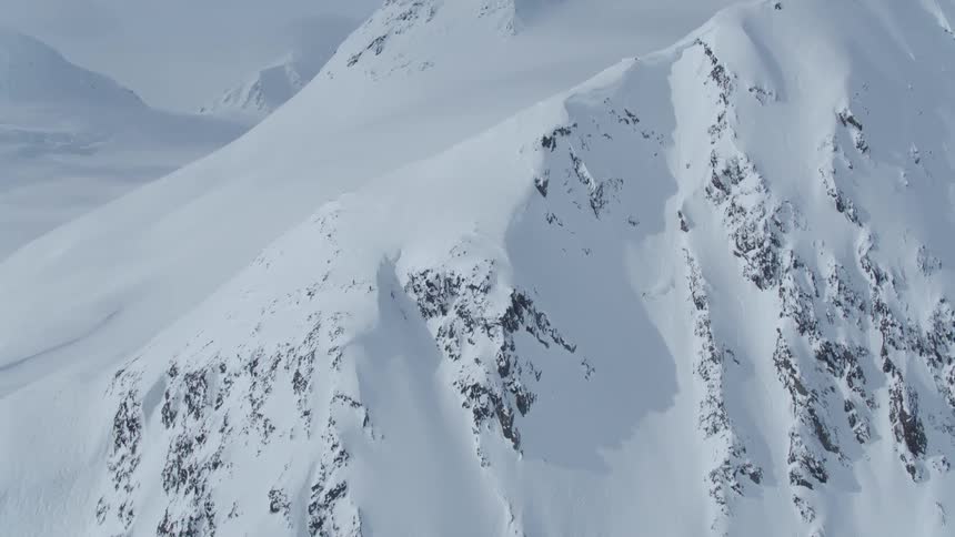A huge stone mountain completely covered in white snow and a person skiing down from the top of the mountain