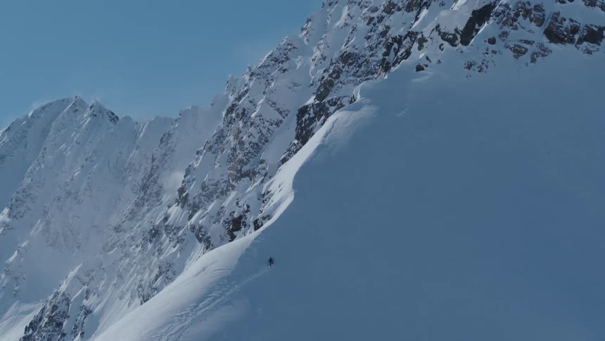 Someone walking up the ridge of a snow covered mountain carrying a snowboard