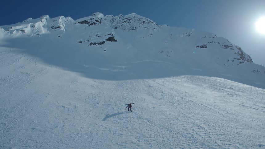 A person is climbing a mountain that is covered with snow on a clear day with a strong sunlight in the sky