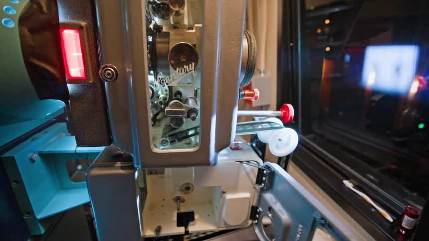 Male projectionist closes the doors on a projection machine operating in the projection booth