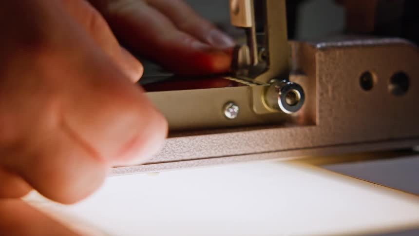 A hand carefully threading a strip of film into the gate of a film projector preparing it for projection