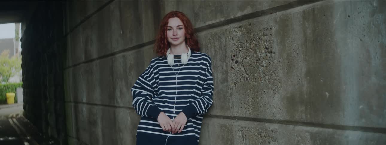 Redheaded woman smiles while leaning against a building