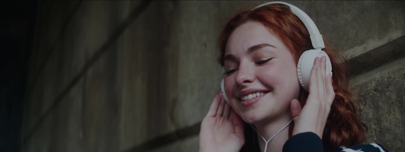 A woman is smiling as she listens to her headphones