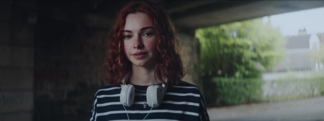 Young redhead woman under an overpass with white headphones