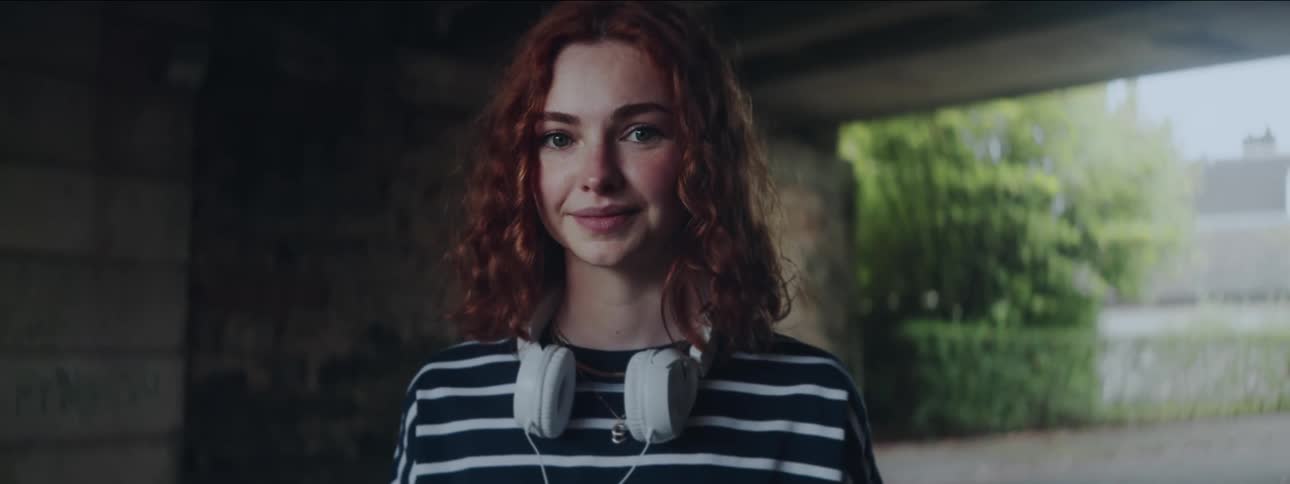 A young woman with red hair smiles directly at the camera