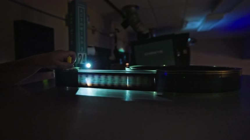 A hand adjusting a film reel on a projector with the film illuminated by a light source
