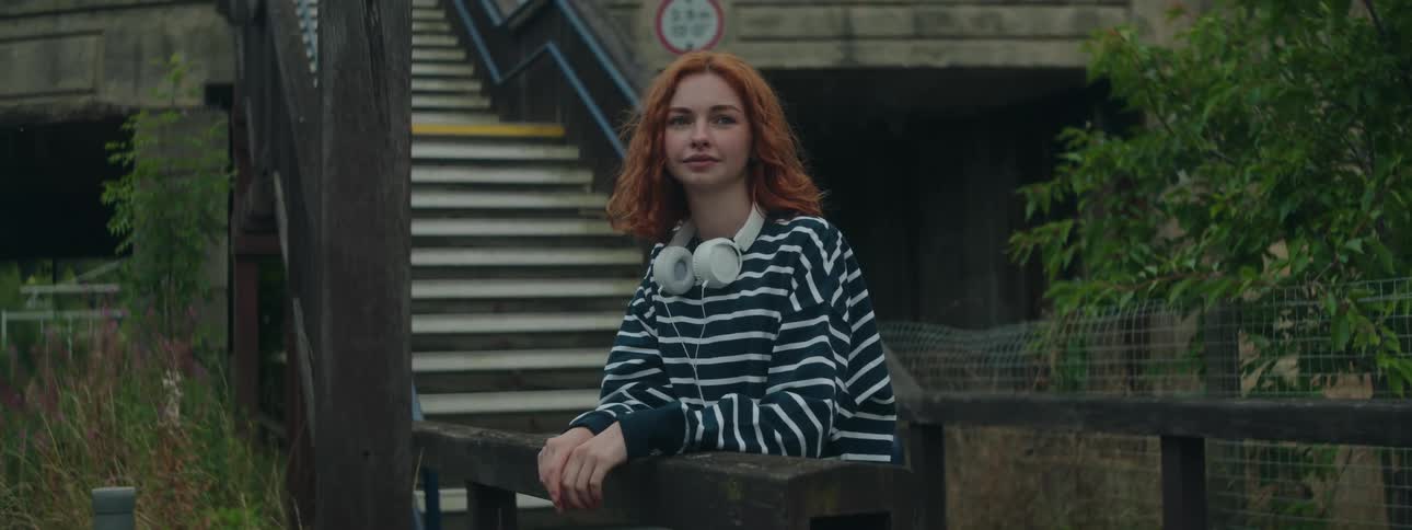 Redheaded woman leaning on a ladder wearing a striped blouse