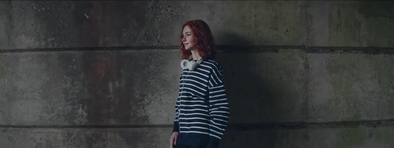 A medium clip of a redhead lady standing close to a concrete wall