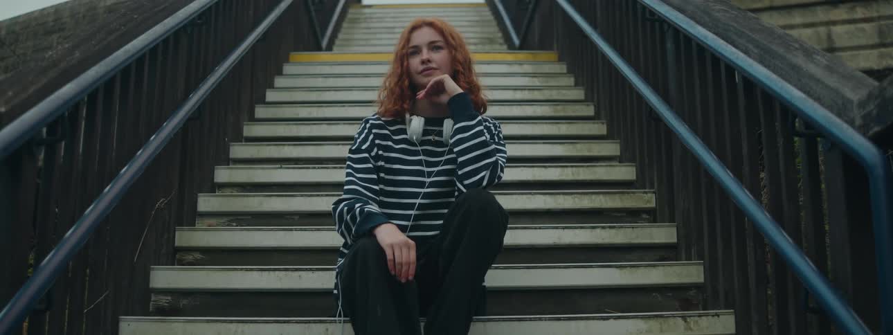 Woman with curly red hair sitting on the stairs of an openair space