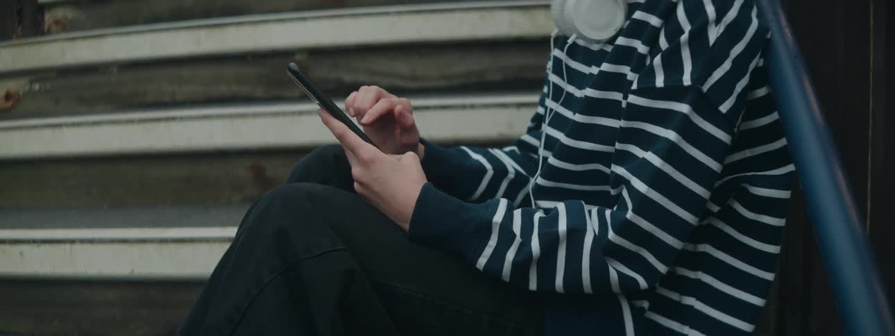 Woman sitting on the steps of a staircase scrolls on her phone
