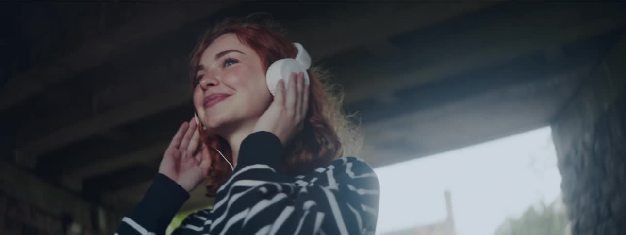A young woman is smiling while having headphones in her ears and she is moving