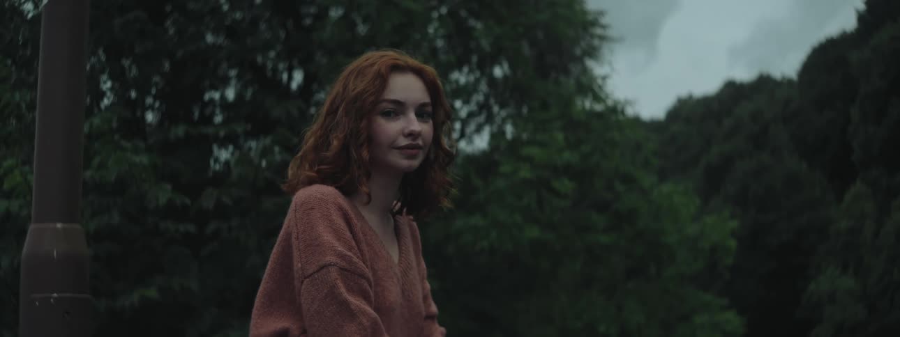A young woman with red hair sits in front of a lush forest