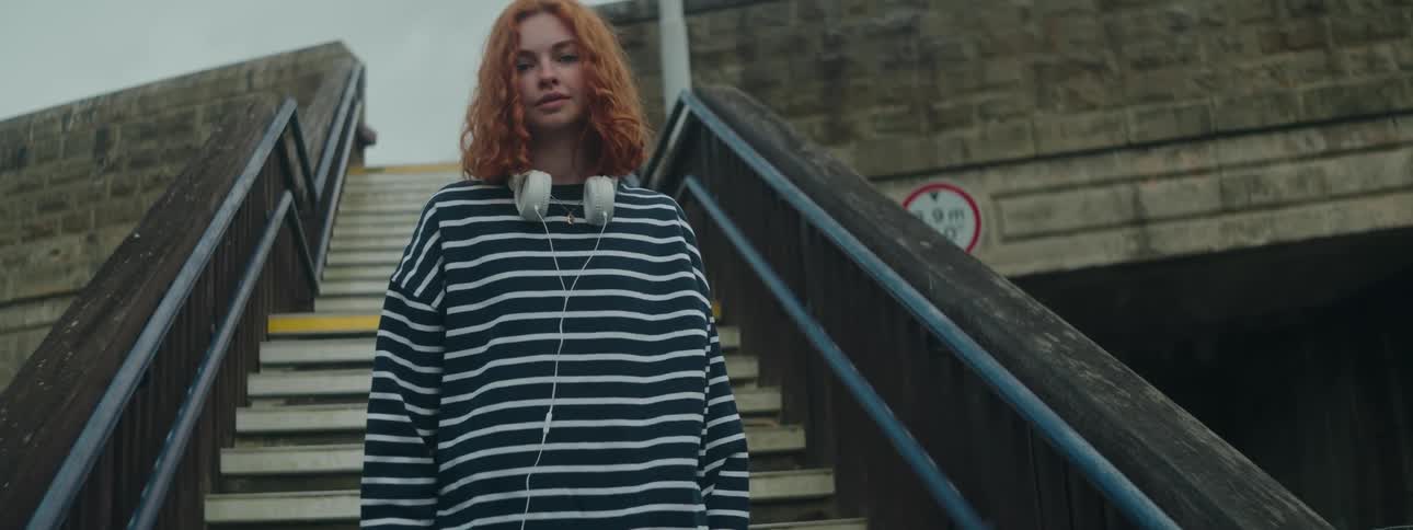 Redheaded woman on the stairs of an open space wearing a striped long sleeve blouse