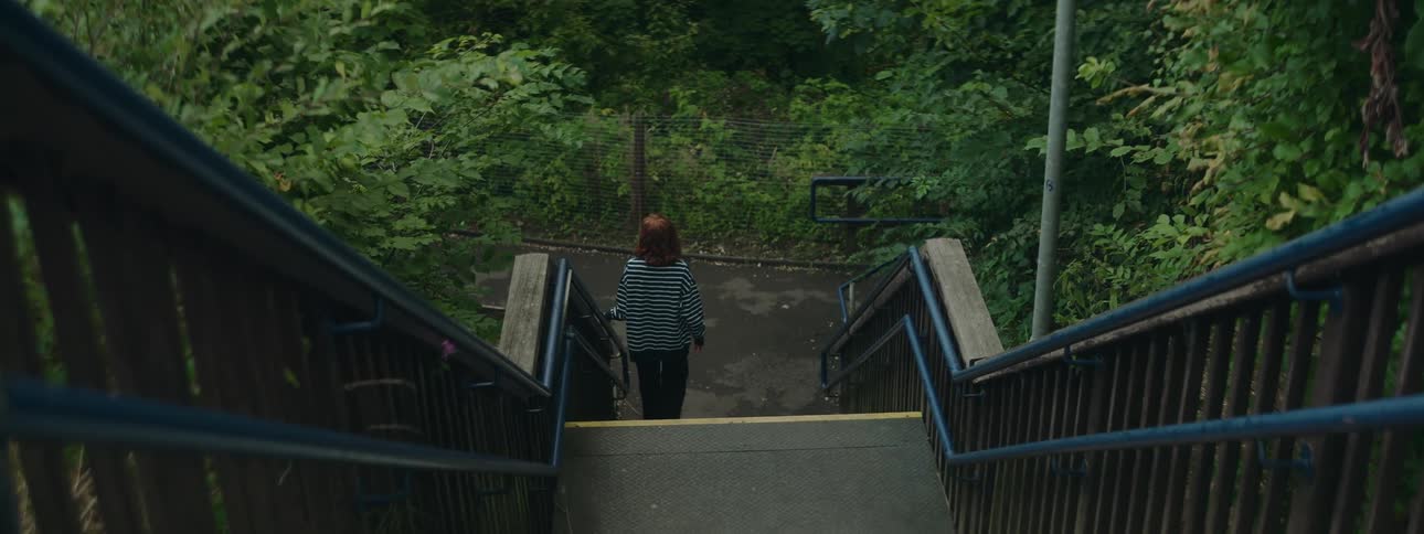 Redheaded female walks down an outdoor staircase near a grove of trees
