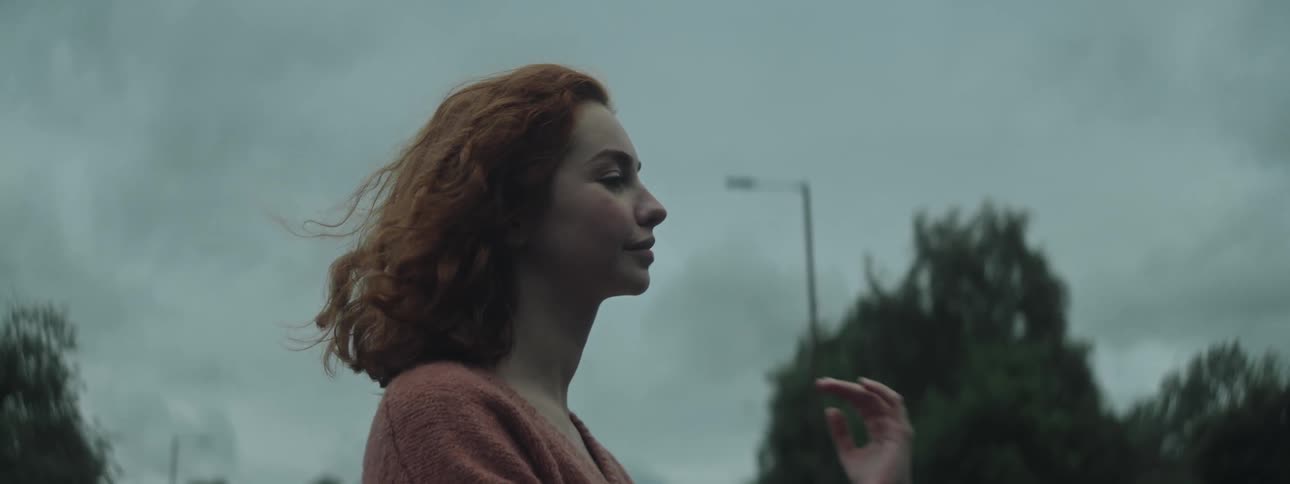 The face of a young woman with curly orange hair and she runs her hand through her hair