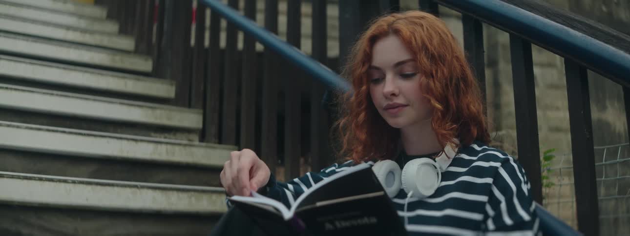 Woman with red hair and striped shirt sitting on steps reading a book