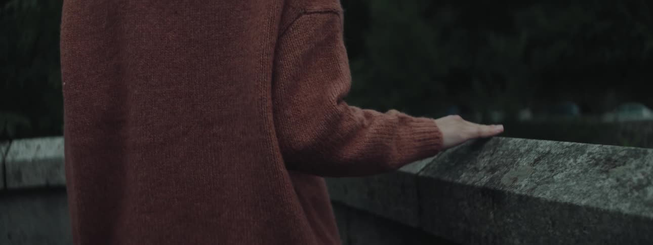 A redheaded woman in a park running her fingers over a small stone brick wall