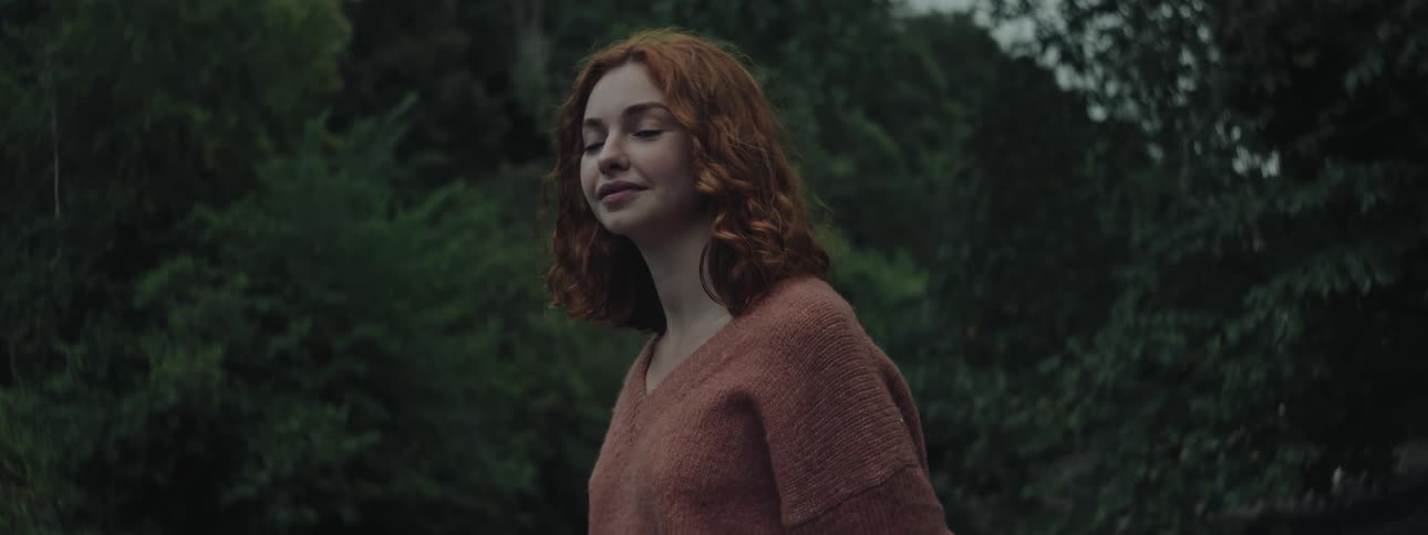 Redhead woman with happy facial expression wearing a red sweater and trees in the background
