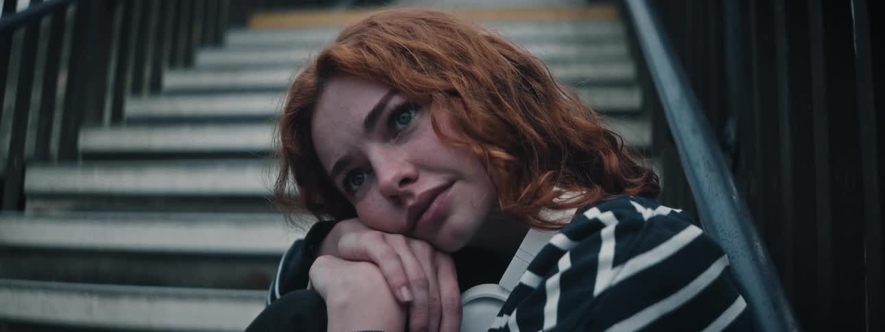 Portrait of a redhaired curlyhaired woman sitting on the stairs with sad facial expression