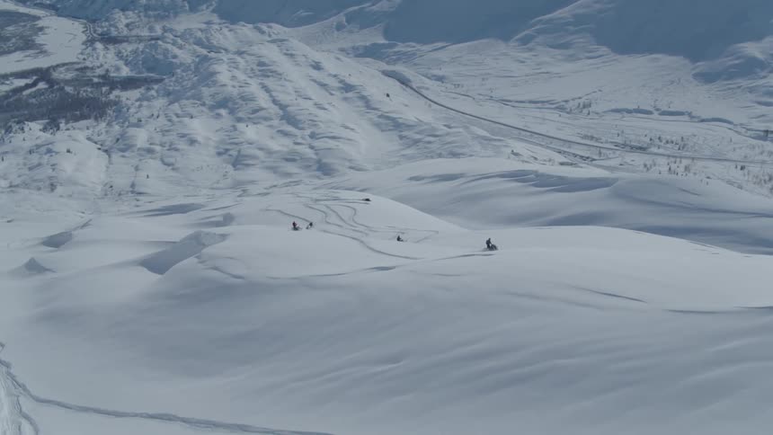Four people on snowmobiles on a snow covered plain near a frozen mountain range